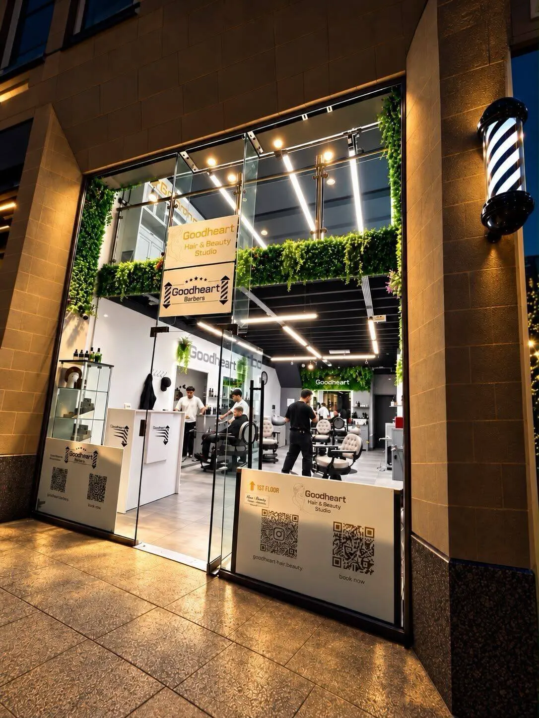 The glass shopfront of Goodheart Studio at Abbey House, Cooper Street, Manchester, with the barber's pole and the shop lit up inside